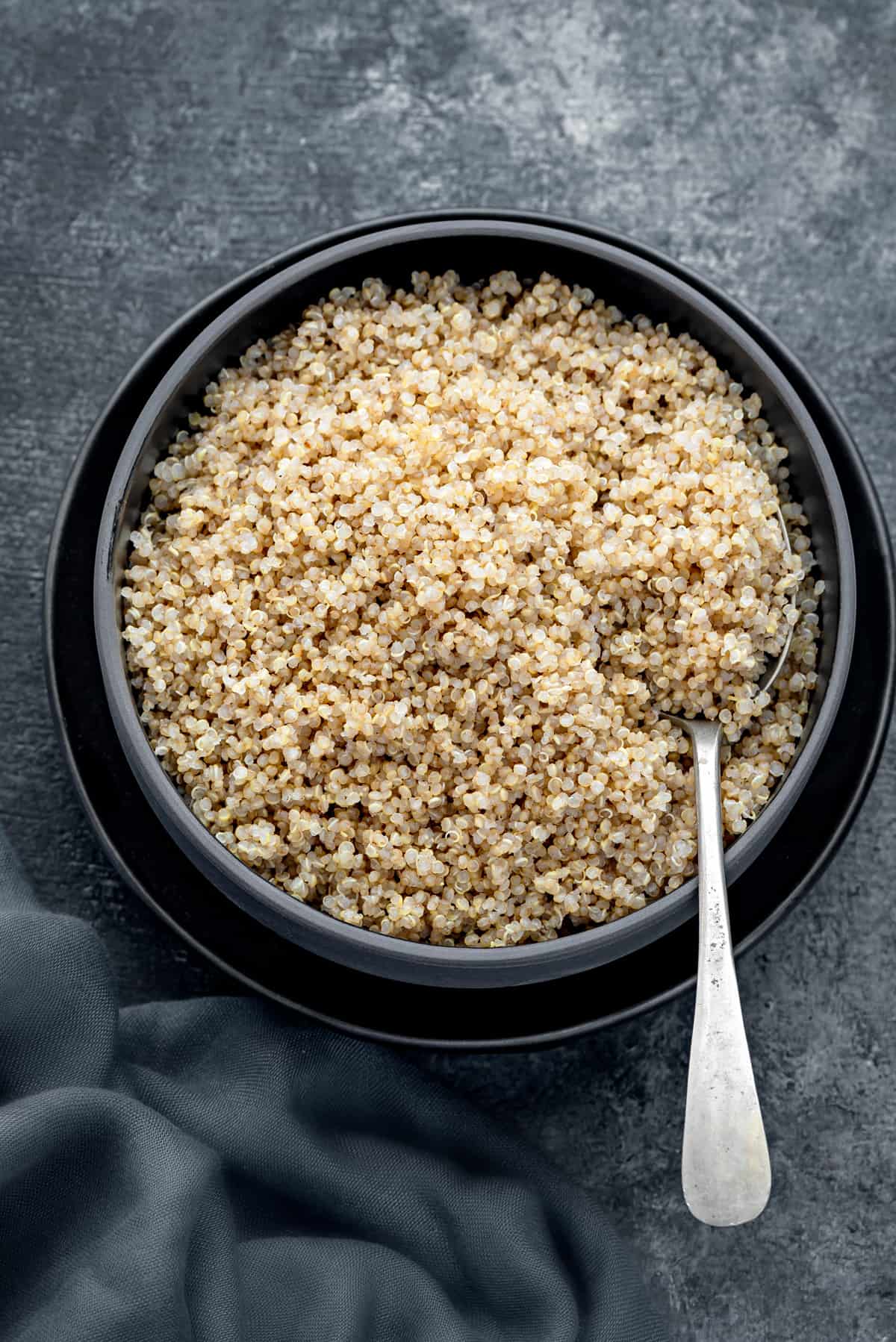 Aerial shot of cooked quinoa in black bowl with spoon side.