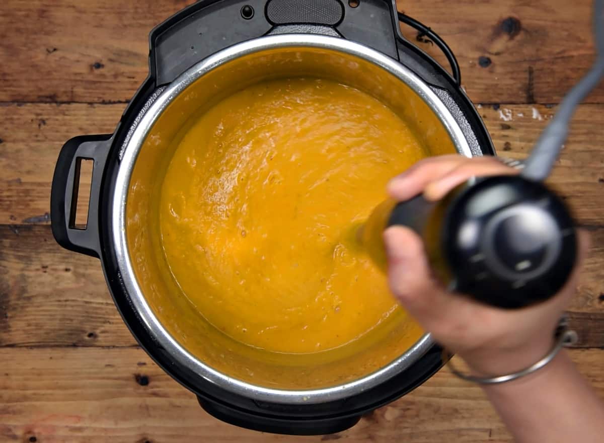 Blending the cooked butternut squash into soup using immersion blender.