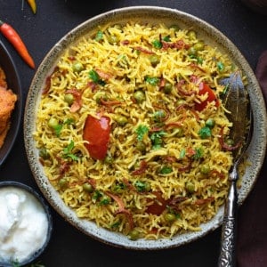 Spicy Instant Pot Matar Pulao served in grey bowl with curd in bowl on side.