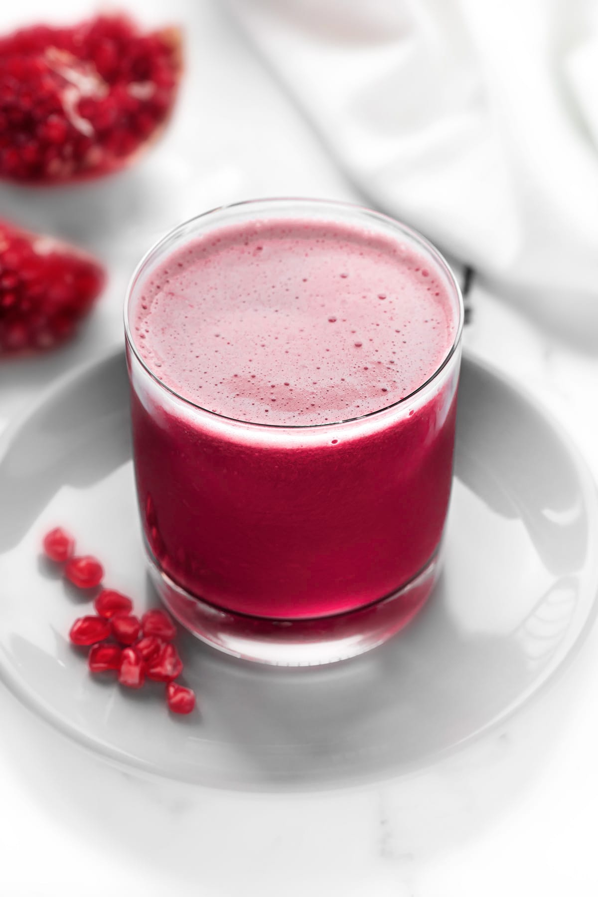 Homemade fresh Pomegranate juice served in glass, few arils spread around and at the back.