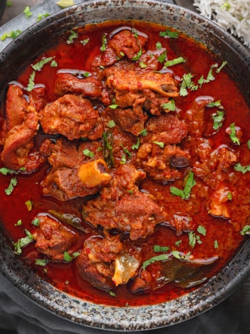Close up shot of lamb vindaloo curry served in black bowl.