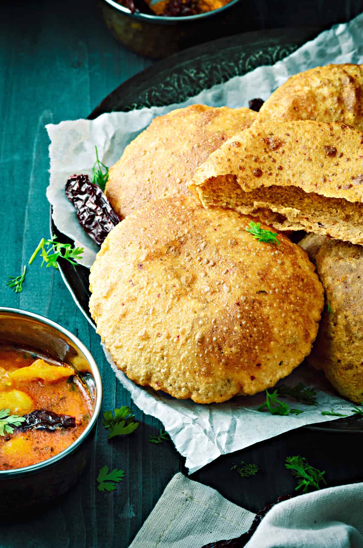 closeup shot of Bedmi Puri with one puri split open along with potato curry on the side.