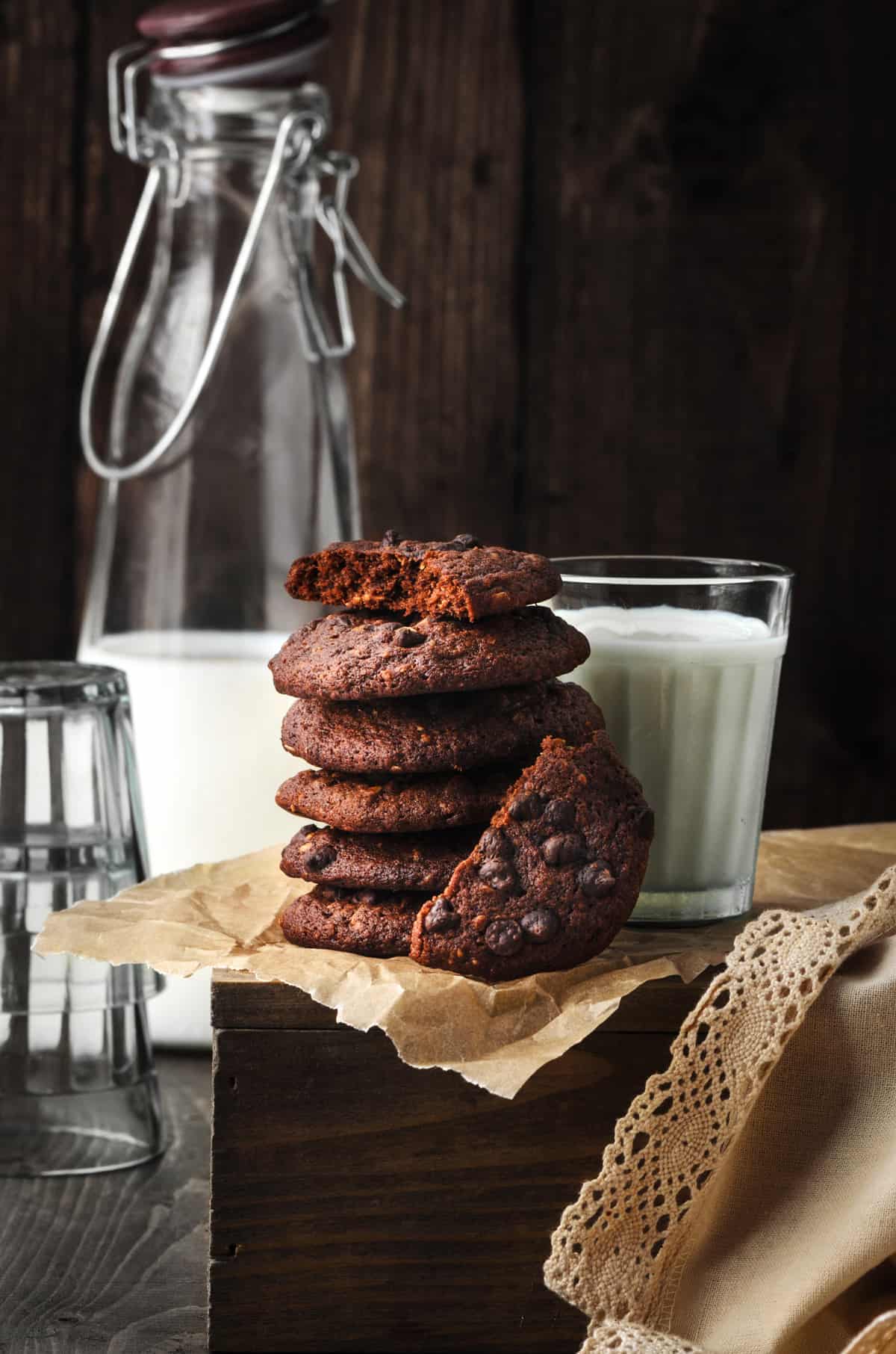 Stacked chocolate chip cookies with a glass of milk bottle and glass at the back.