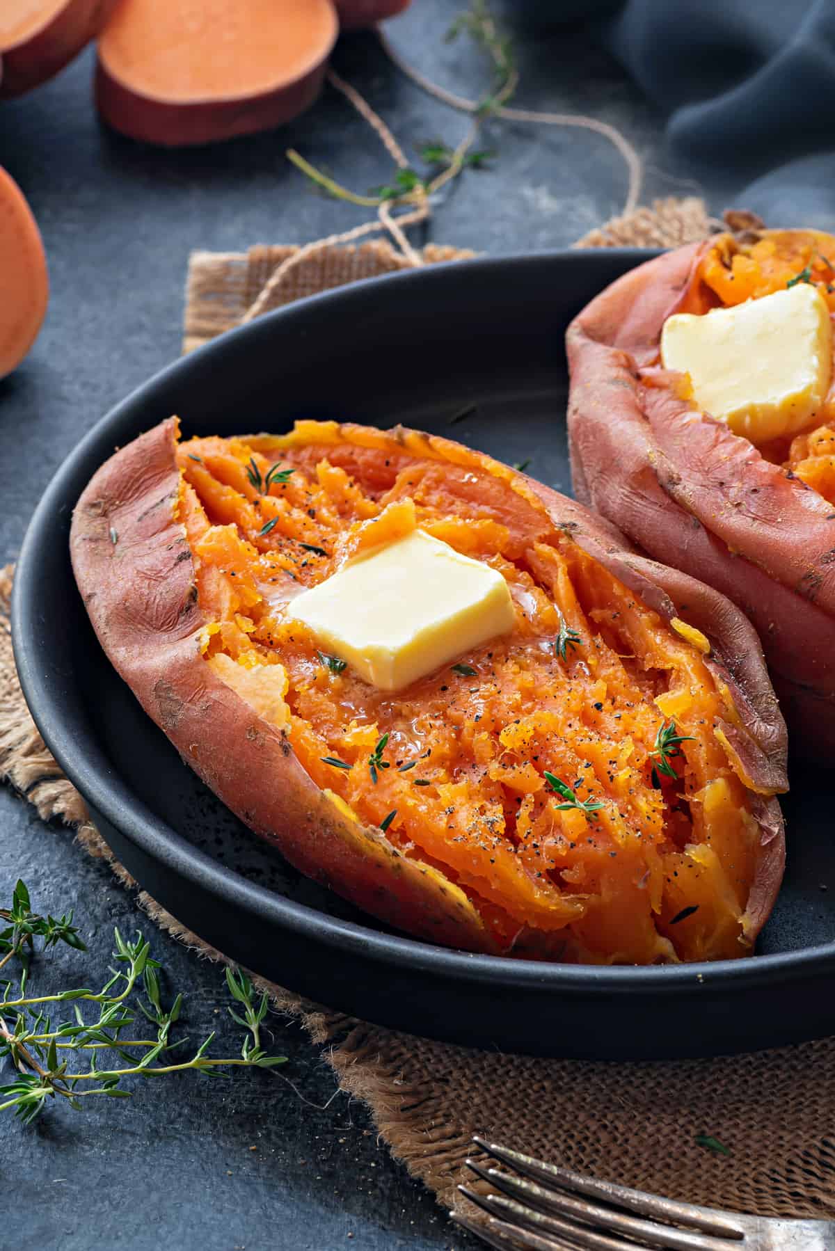 Close up shot of steamed Instant Pot sweet potatoes with butter cube on black plate.