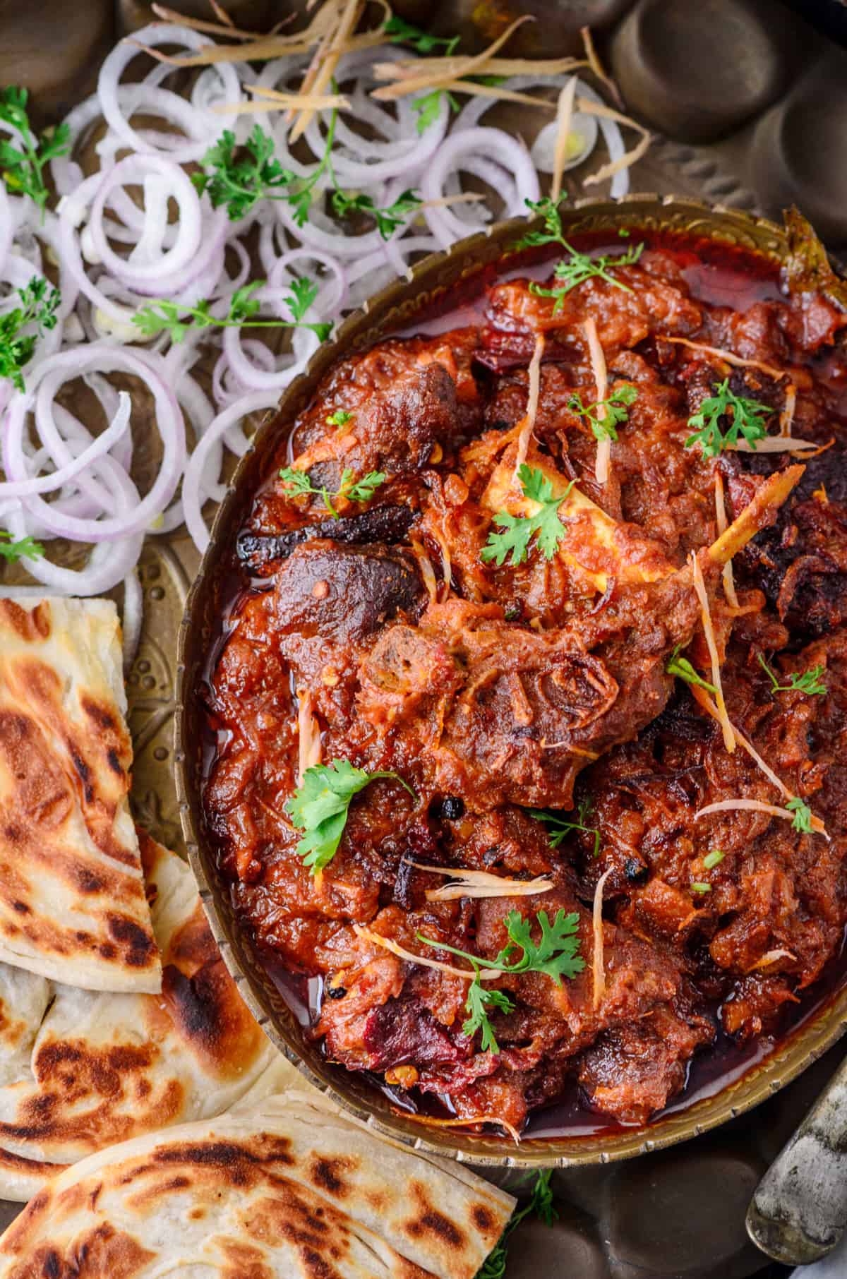 Close up shot of Bhuna Gosht in brass platter with parathas on side.