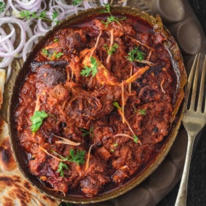 Bhuna Gosht served in brass plate served with parathas on side.