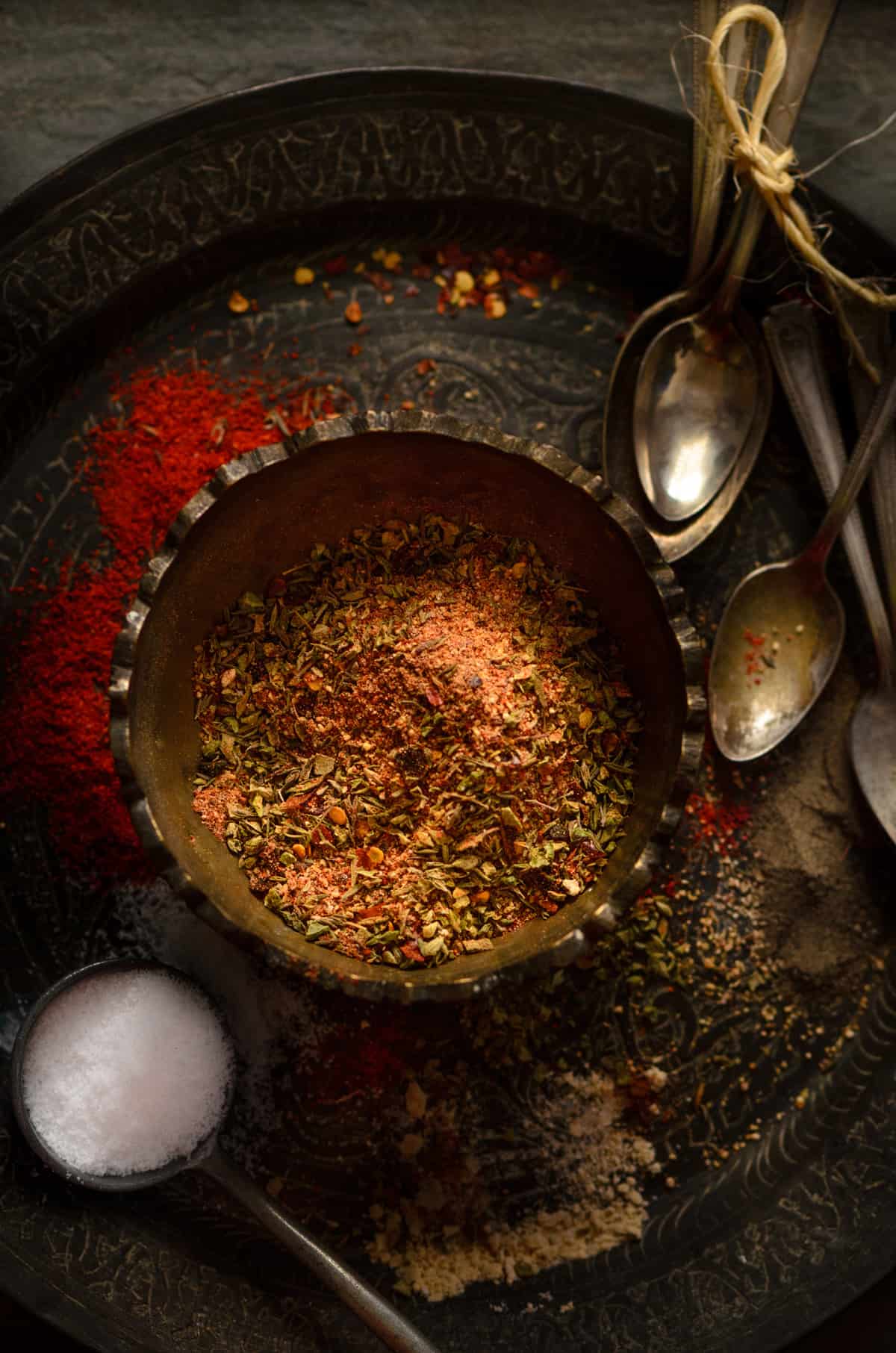 Cajun spice mix in brass bowl kept on plate with salt and spices spread around.