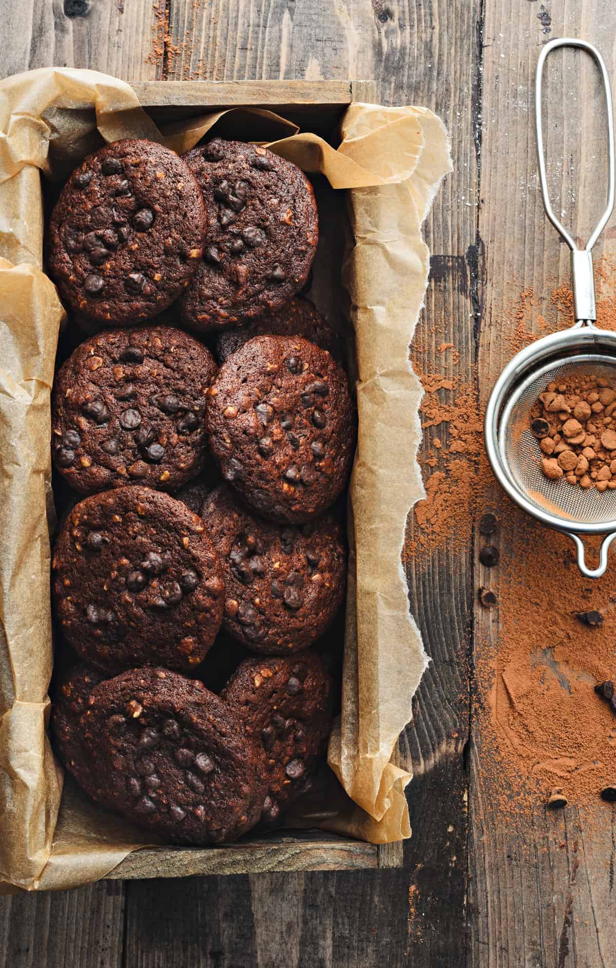 Chocolate chips oats cookies placed in rectangular wooden box with cocoa powder spread around.