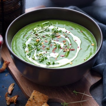 Garnished green pea soup in two brown bowls with croutons on the side.