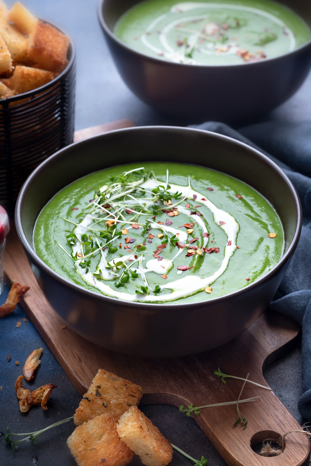 Close up shot of green peas soup in 2 brown bowls with croutons on side.