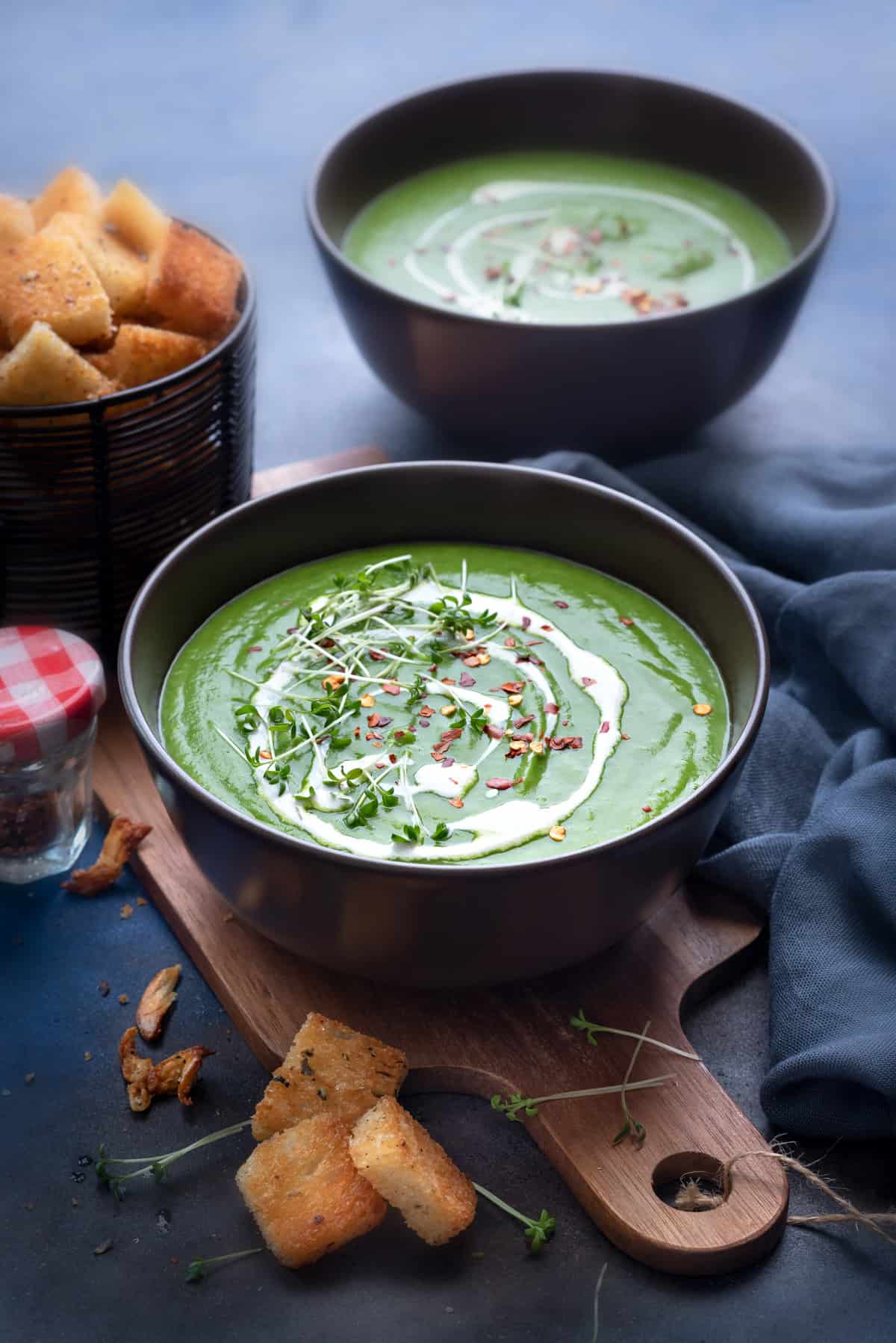 Garnished green pea soup in two brown bowls with croutons on the side.