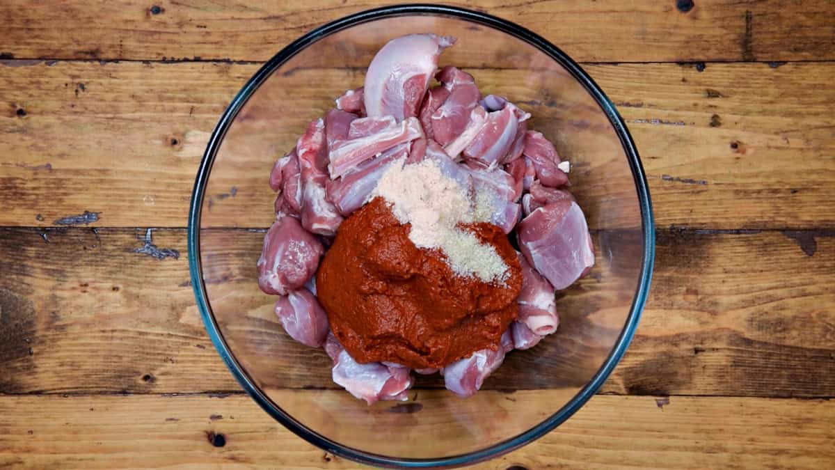 Vindaloo curry paste, salt and sugar added to lamb in a glass bowl.