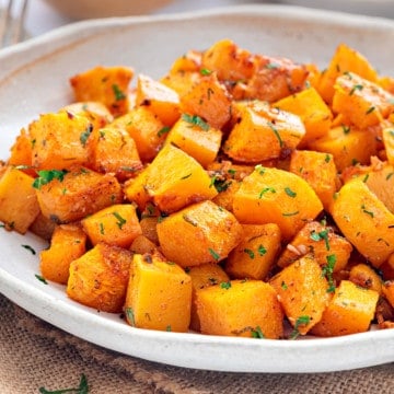 Closeup of roasted butternut squash in white ceramic plate.