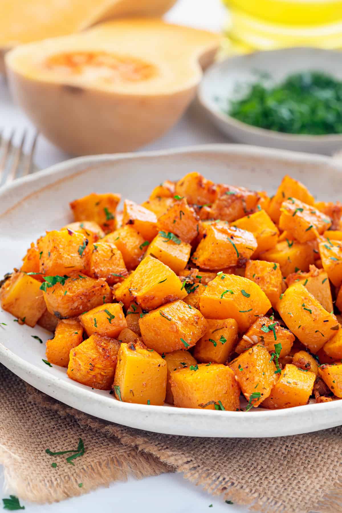 Roasted butternut squash cubes in white ceramic plate.