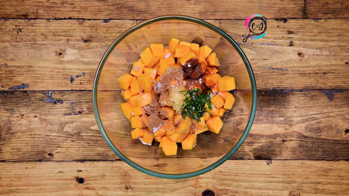 All the savory ingredients added to butternut squash cubes placed in bowl.