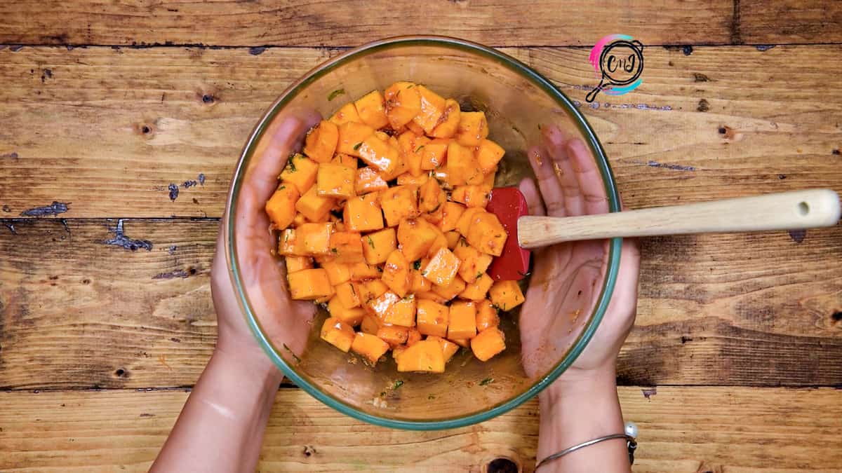 Butternut squash cubes tossed well in seasonings in bowl.