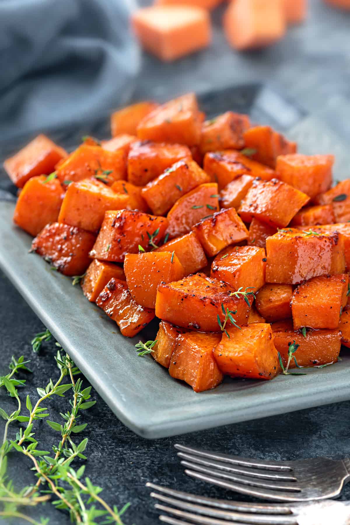 A plate of cubed, caramelized, sweet potatoes with sprigs of thyme on top.