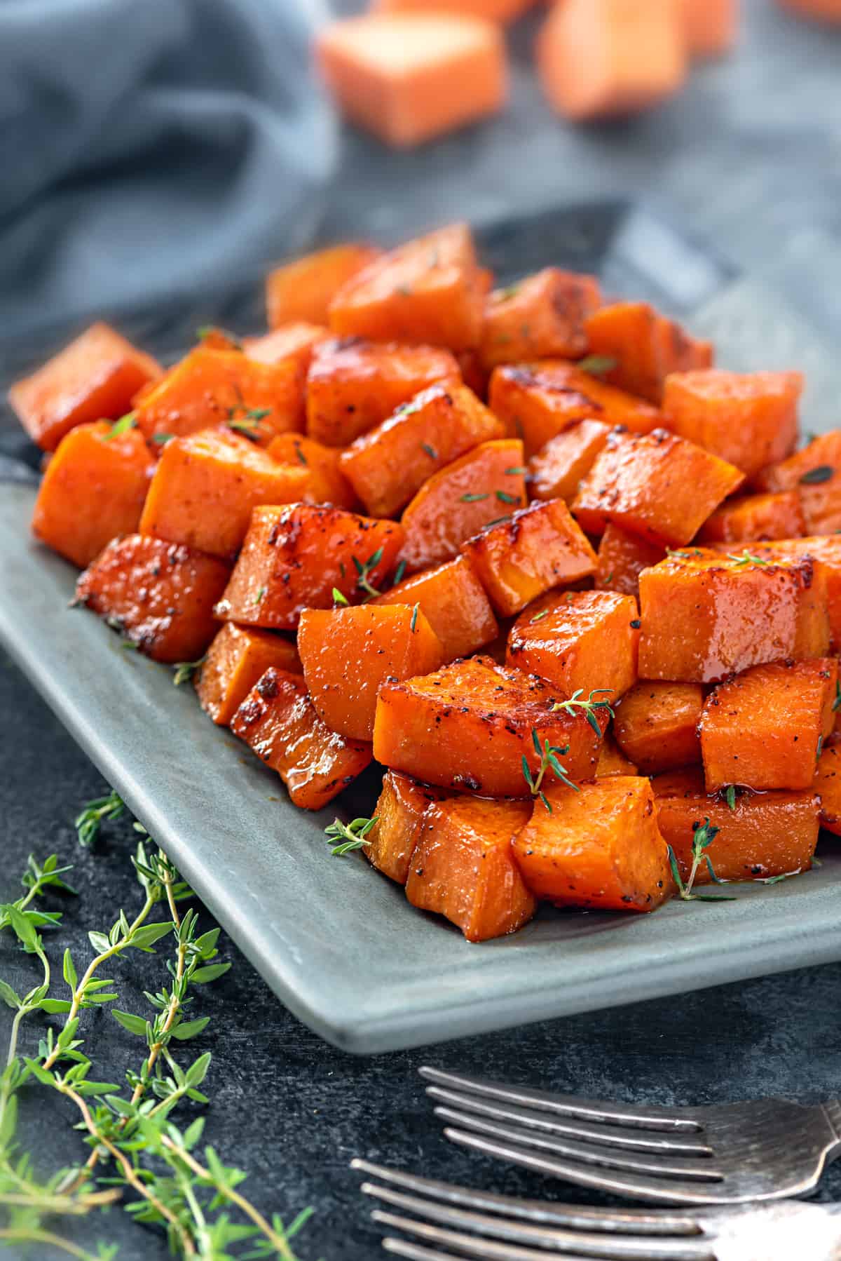 A plate of cubed, caramelized, sweet potatoes with sprigs of thyme on top. 