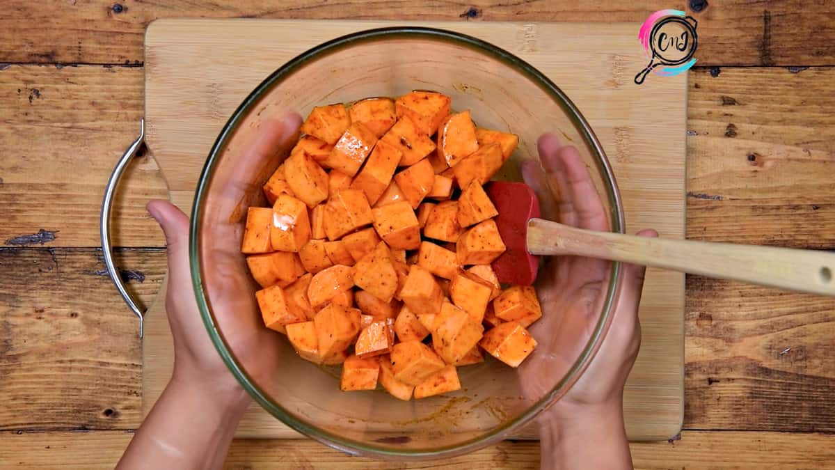 Sweet potato tossed with maple and seasonings in glass bowl.