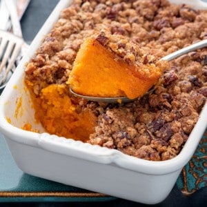 Closeup shot of spoon holding sweet potato casserole that is kept on casserole dish.