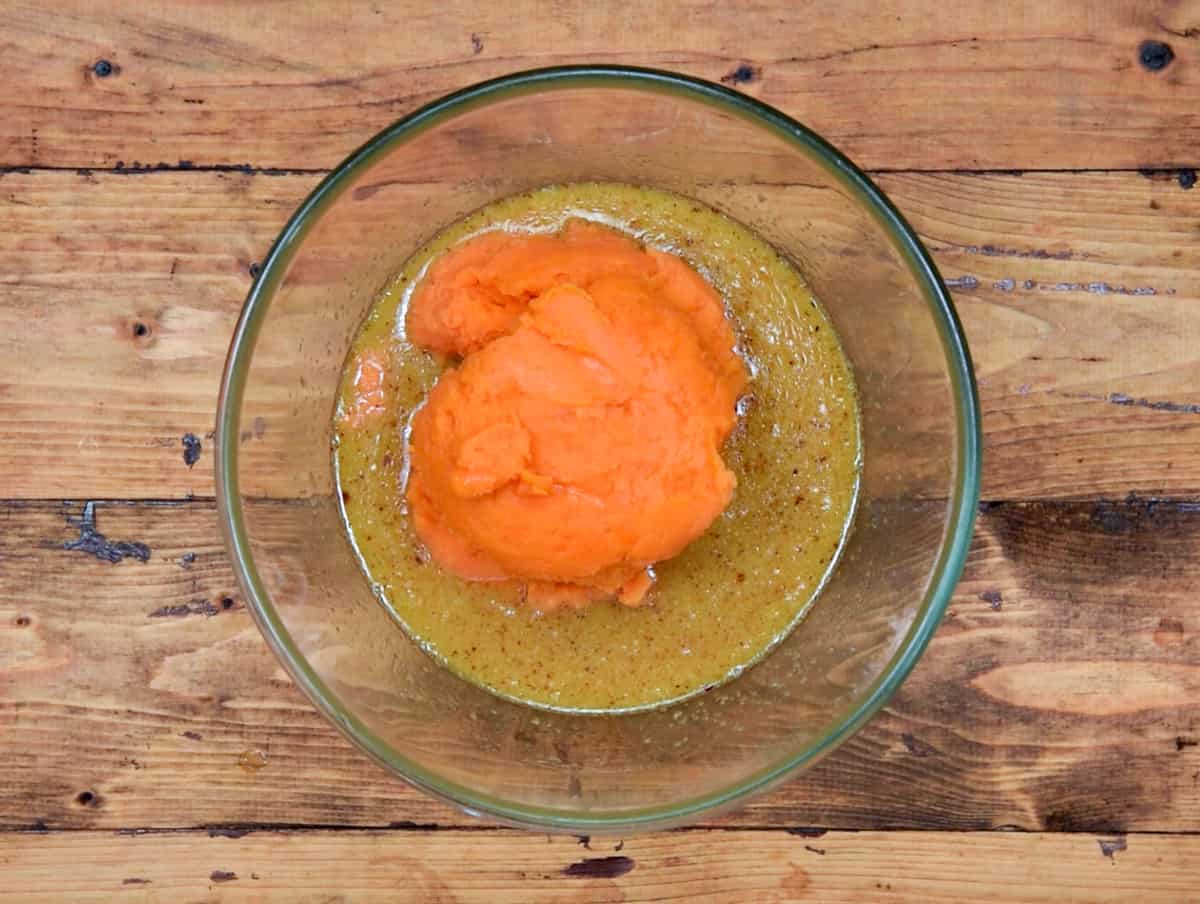 Mashed sweet potatoes added to whisked egg butter mixture in glass bowl.