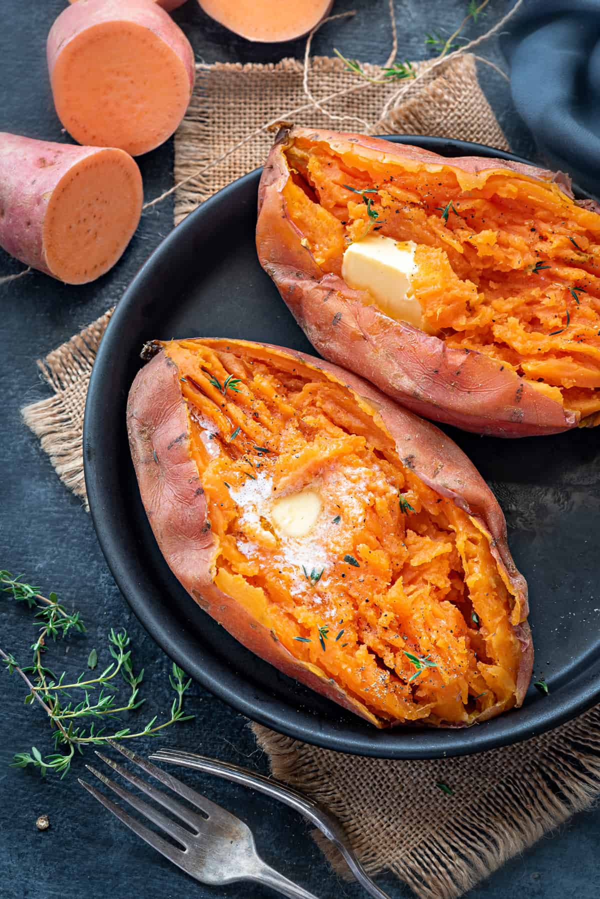 Side angle shot of two steamed sweet potatoes mashed with melted butter on black plate.