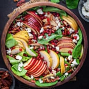 Completed arugula apple pear pomegranate harvest fall salad in wooden serving bowl.