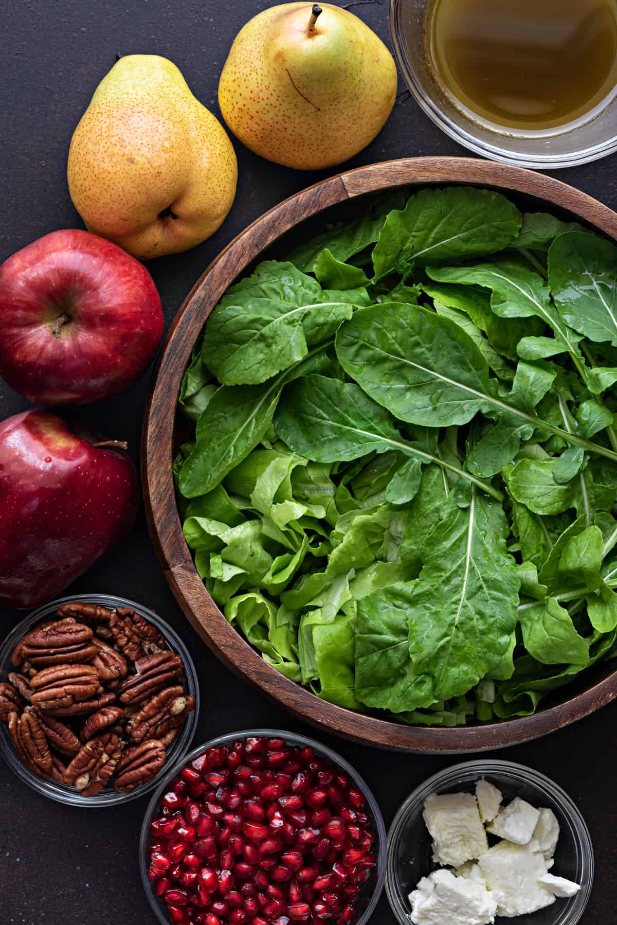 fresh spinach and rocket mix in a wooden bowl with fall salad mis en place surrounding it