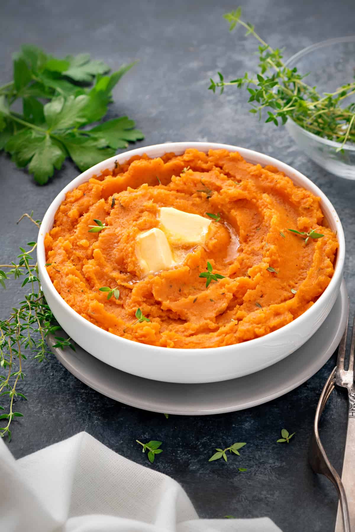 white bowl with mashed sweet potatoes topped two pats of butter and fresh thyme leaves. 