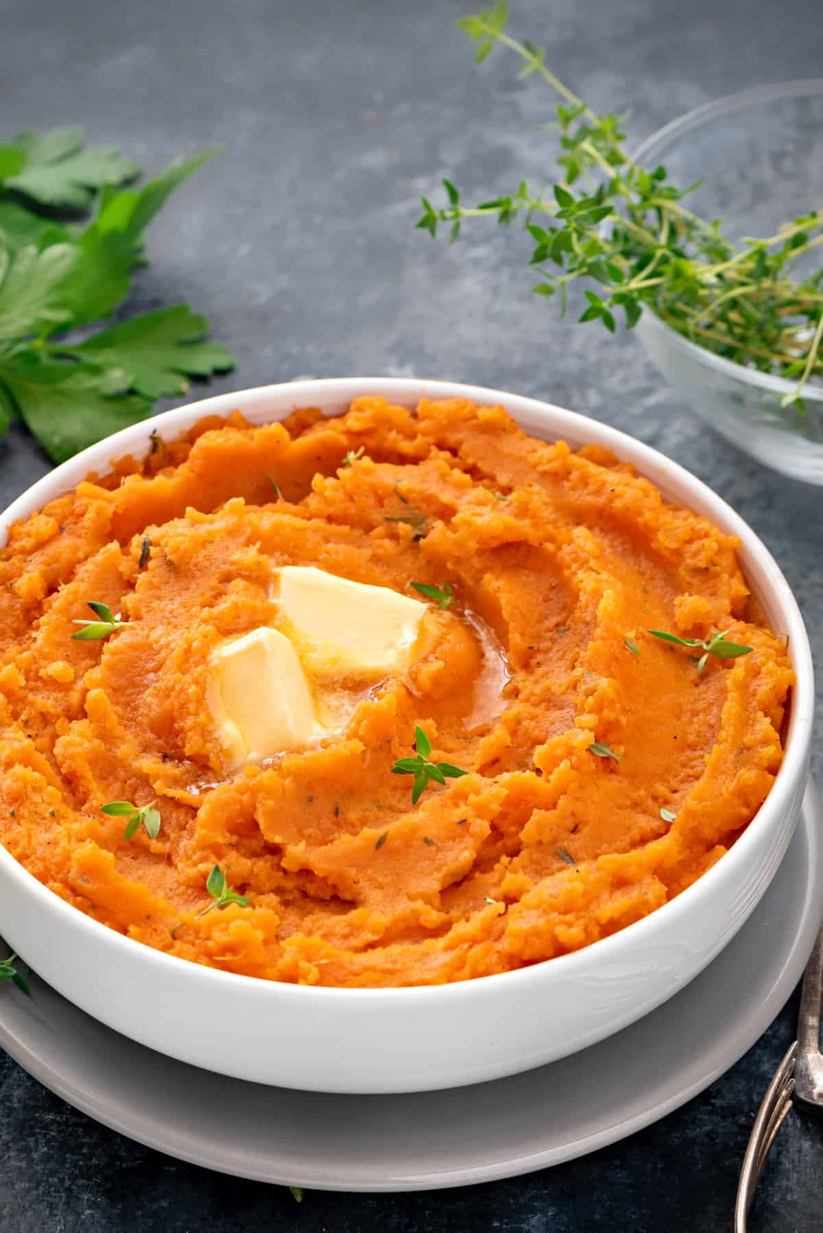 white bowl filled with mashed sweet potatoes topped with pats of butter and fresh thyme