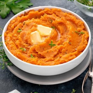 mashed sweet potatoes in a white bowl topped with butter and fresh herbs