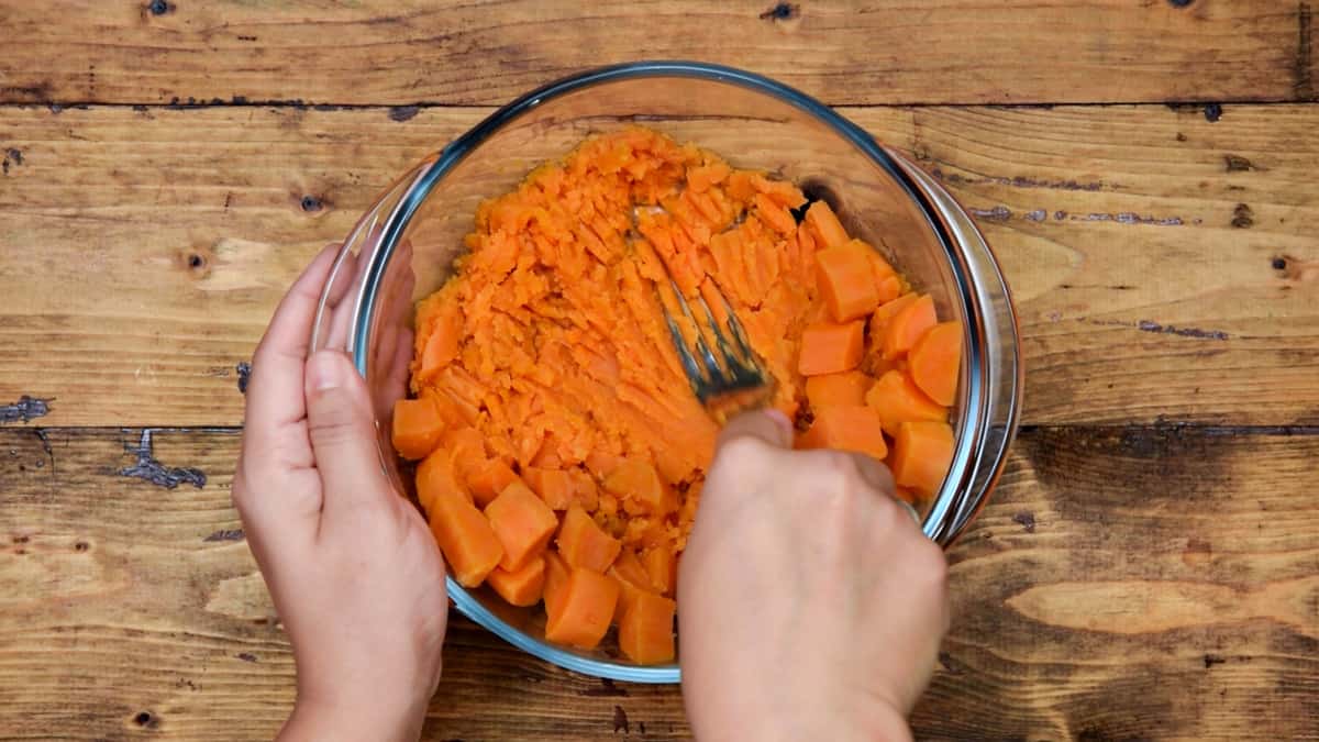 cooked sweet potato cubes being mashed with a fork