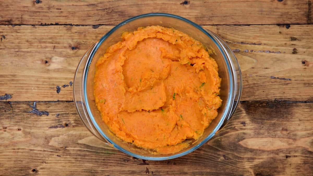 completed mashed sweet potatoes in a clear glass bowl on a wood background