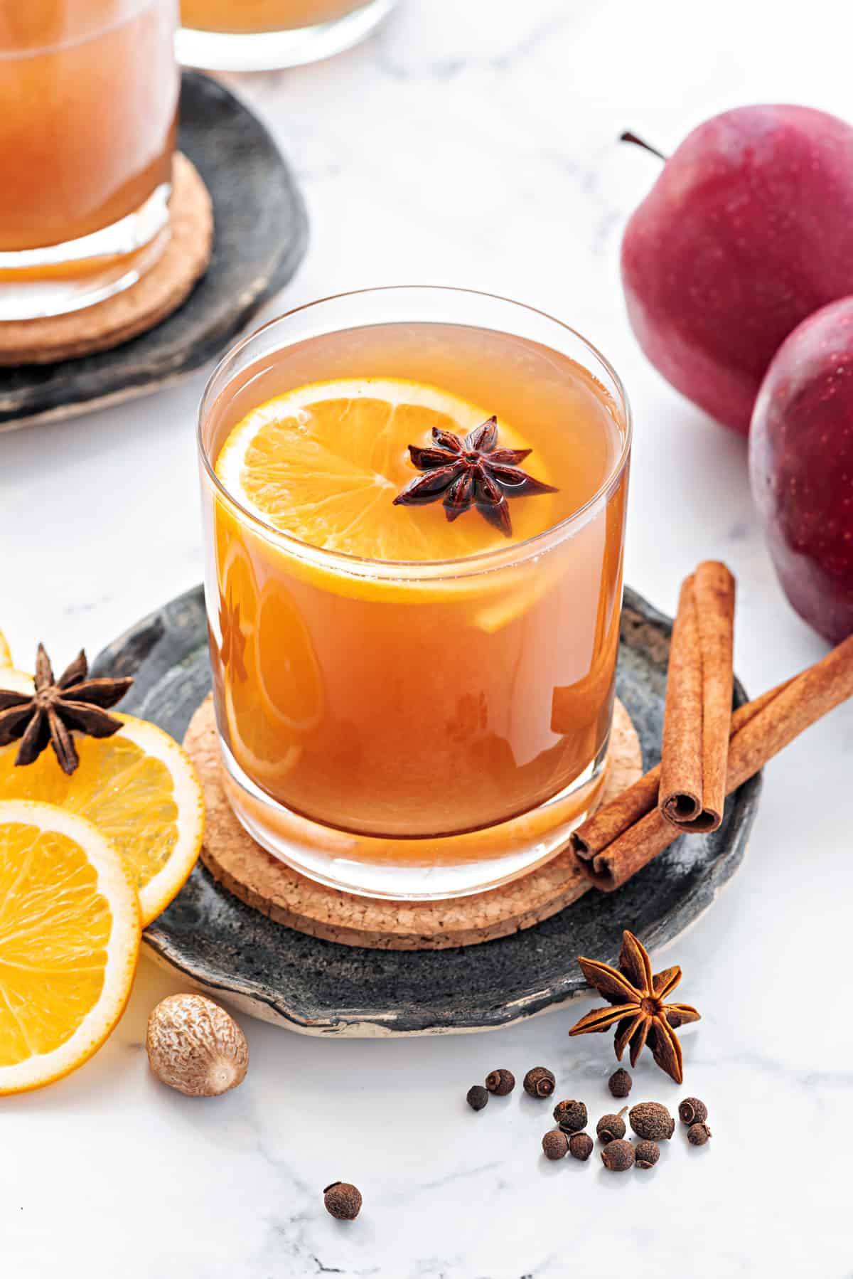 Apple cider drink in a glass, some whole spices spread around and apples placed on side