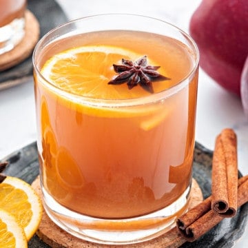 Closeup shot of homemade apple cider drink served in glass, some whole spices spread around