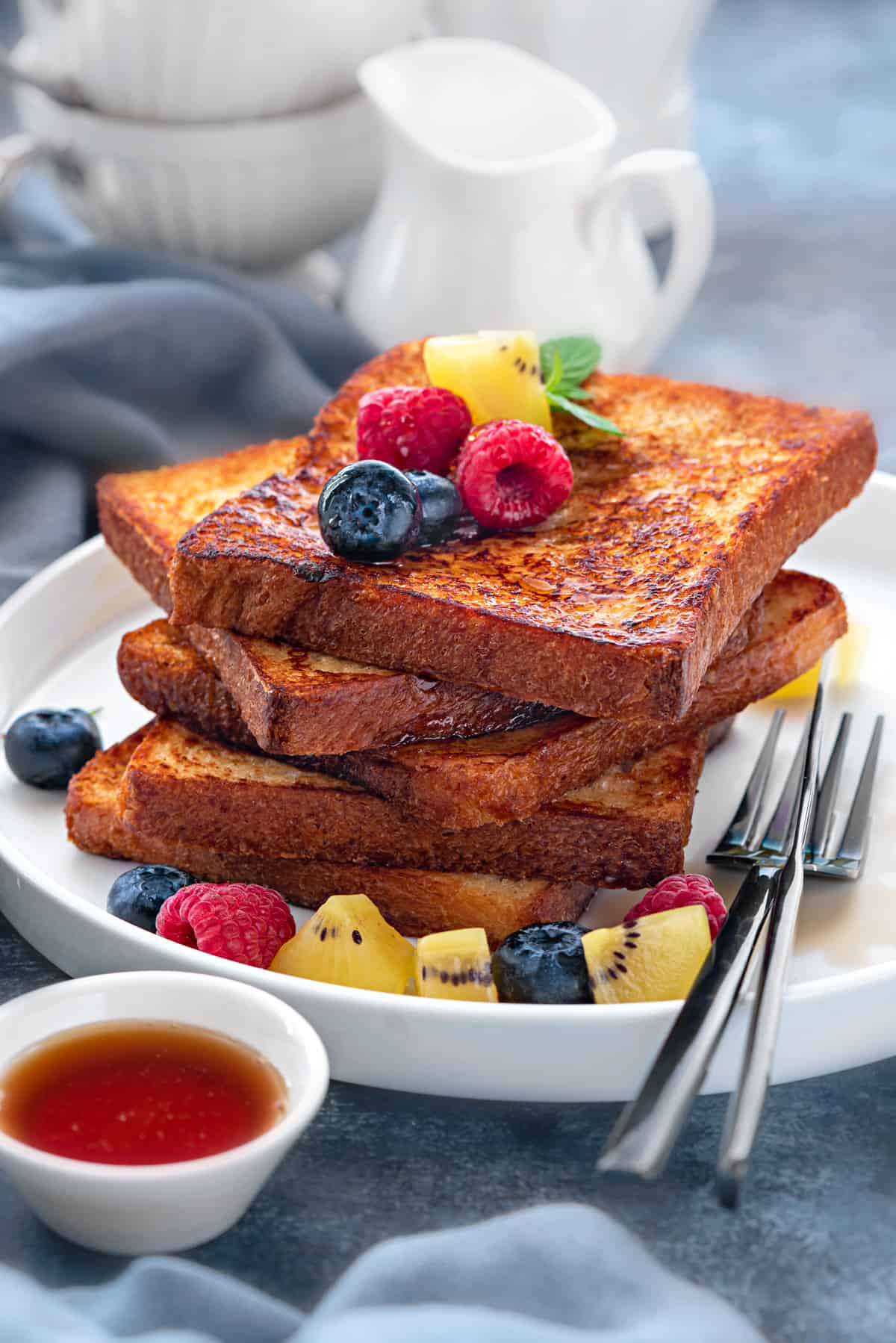 Stack of 5 slices of brioche french toast on a white plate topped with fresh fruits.