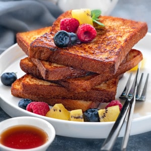 Stack of 5 slices of brioche french toast on a white plate topped with fresh fruits