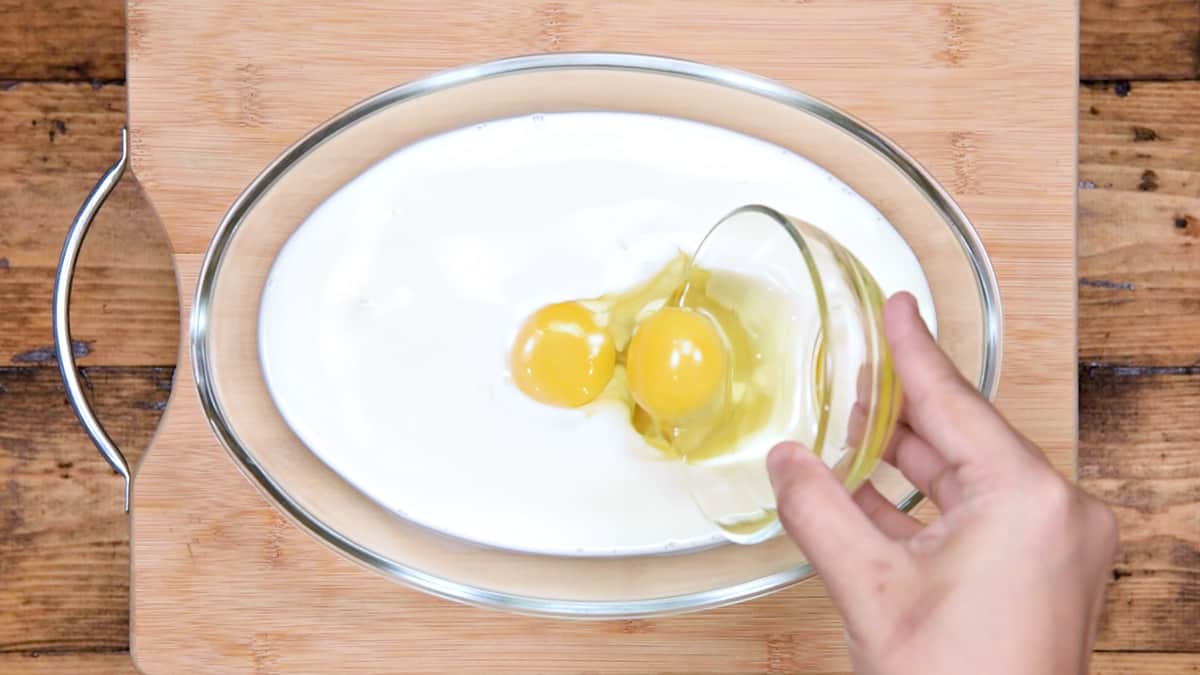 hand pouring eggs into milk in a mixing dish