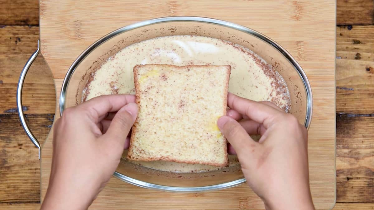 hands removing a piece of soaked bread from custard mixture