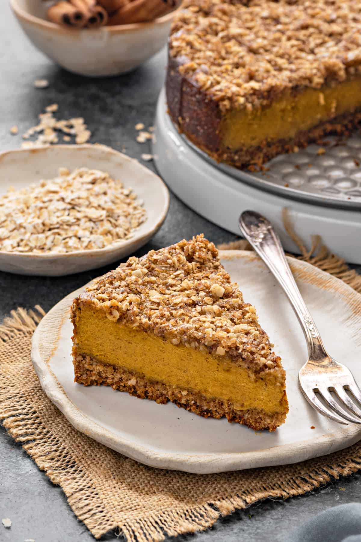 slice of gluten free pumpkin cheesecake on a white plate with a silver fork and the rest of the cheesecake in the background