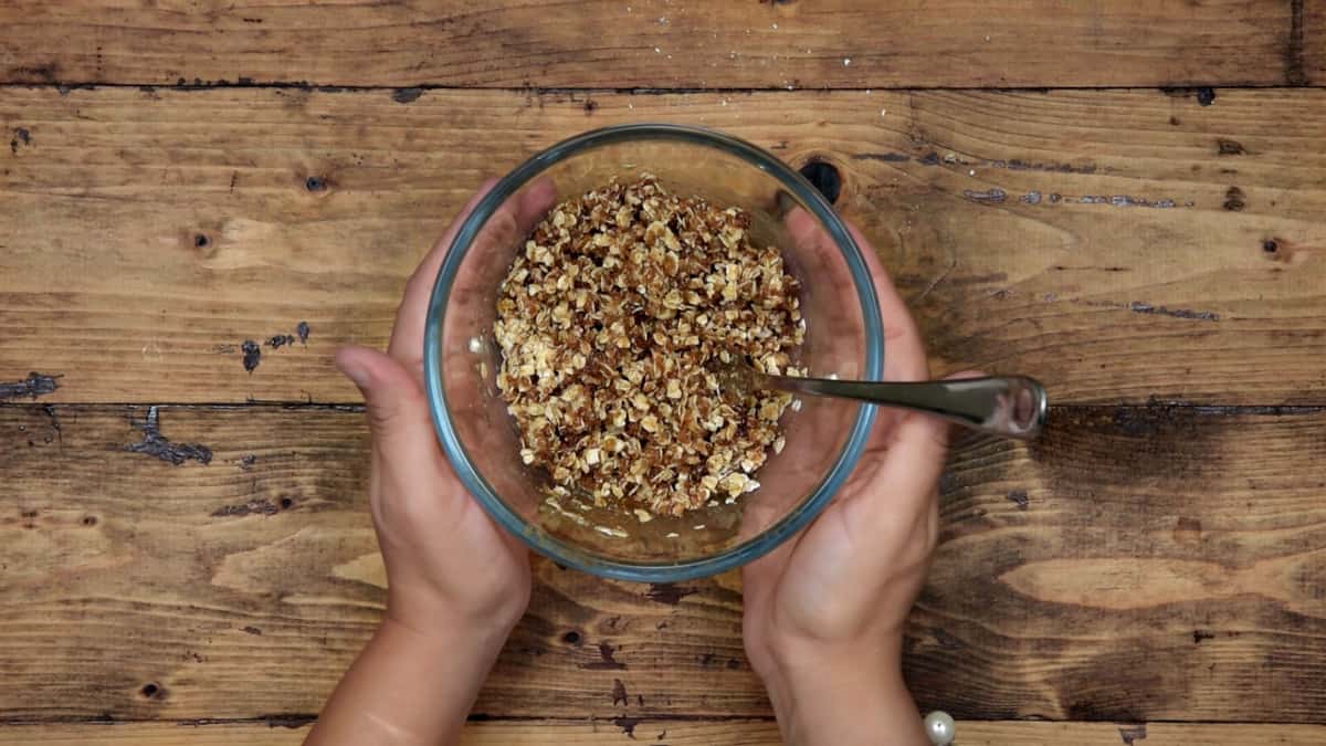 two hands holding a mixing bowl with oat crumble topping