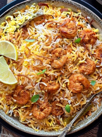 Closeup of Prawn biryani served in ceramic bowl with spoon into it.