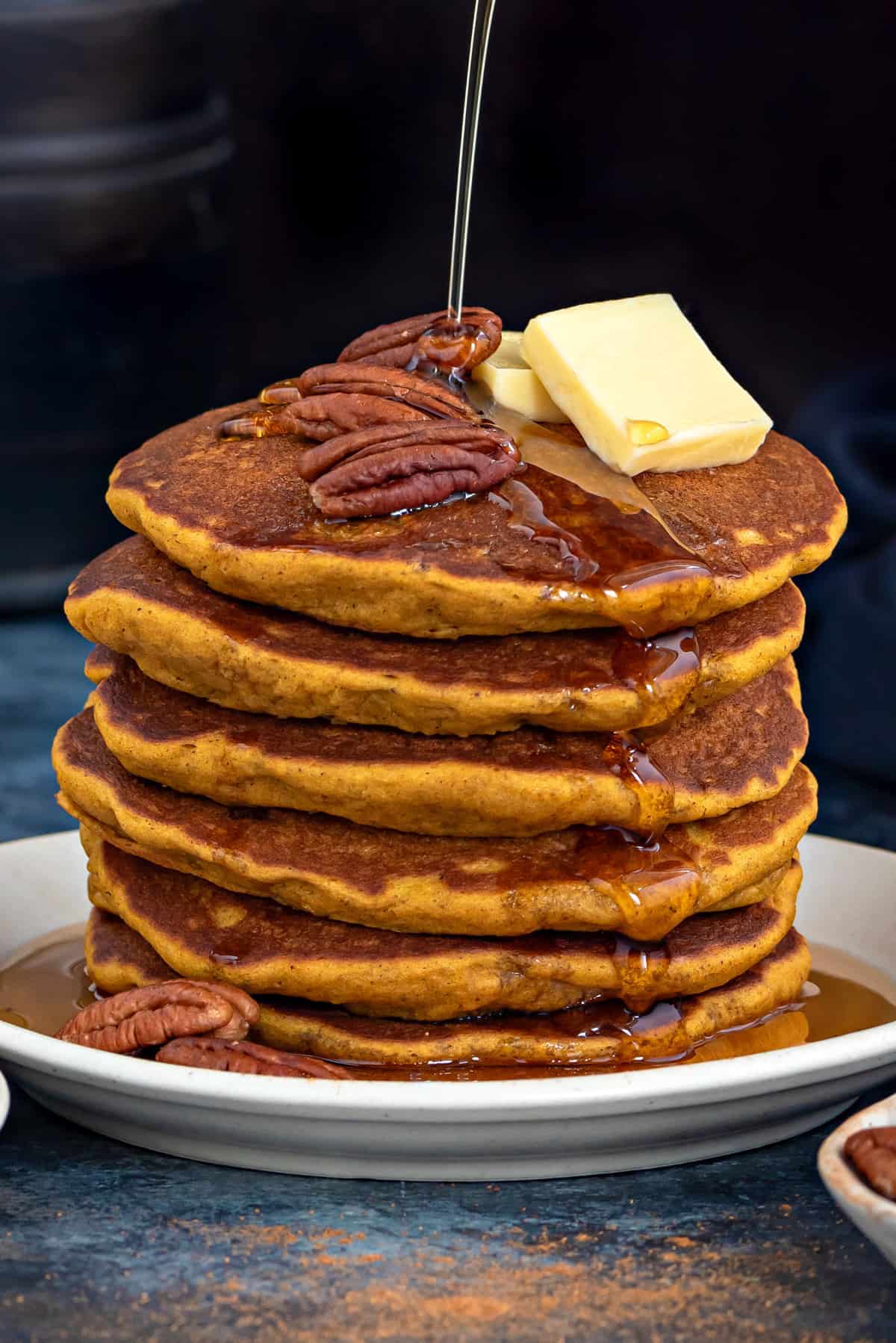 Short stack of healthy pumpkin pancakes topped with pads of butter, pecans and maple syrup