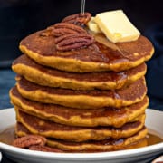 Short stack of healthy pumpkin pancakes topped with pads of butter, pecans and maple syrup