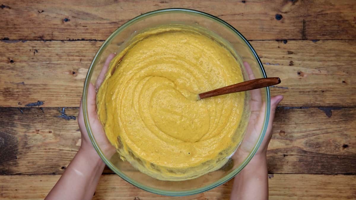 two hands holding mixing bowl filled with pumpkin spice pancake batter