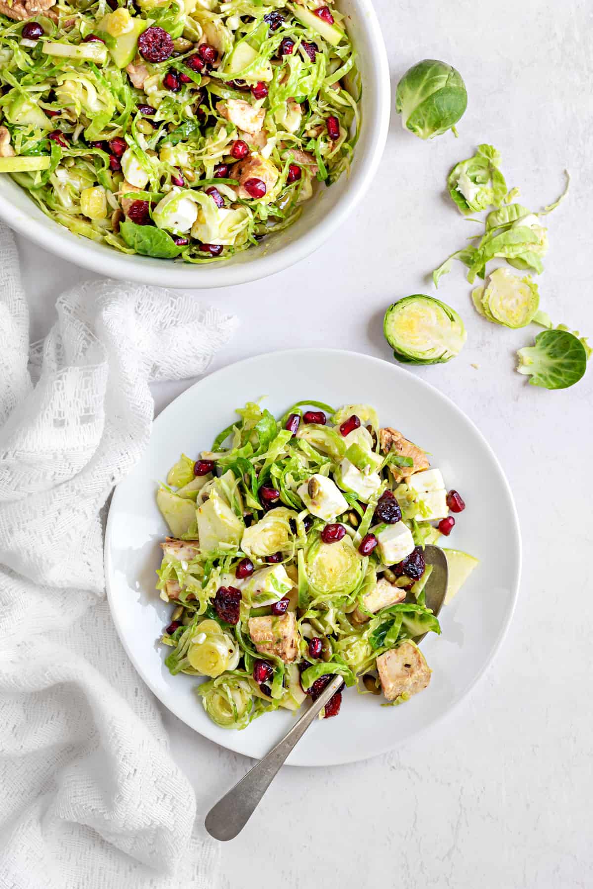 Shaved brussel sprout salad with chicken, pomegranate, cranberries, seeds and feta served on a white plate