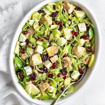 Overhead shot of shaved brussels sprouts salad in a white oblong serving dish on a white tabletop with a white linen and a silver spoon