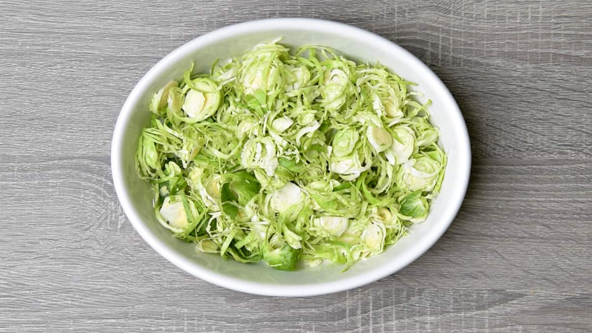 raw shaved brussel sprouts in a white oval dish