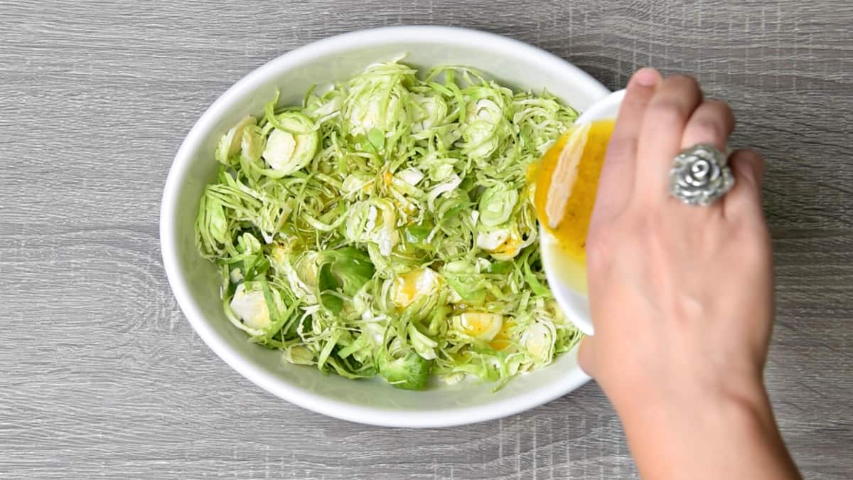 hand pouring apple cider vinaigrette over shredded raw brussels sprouts