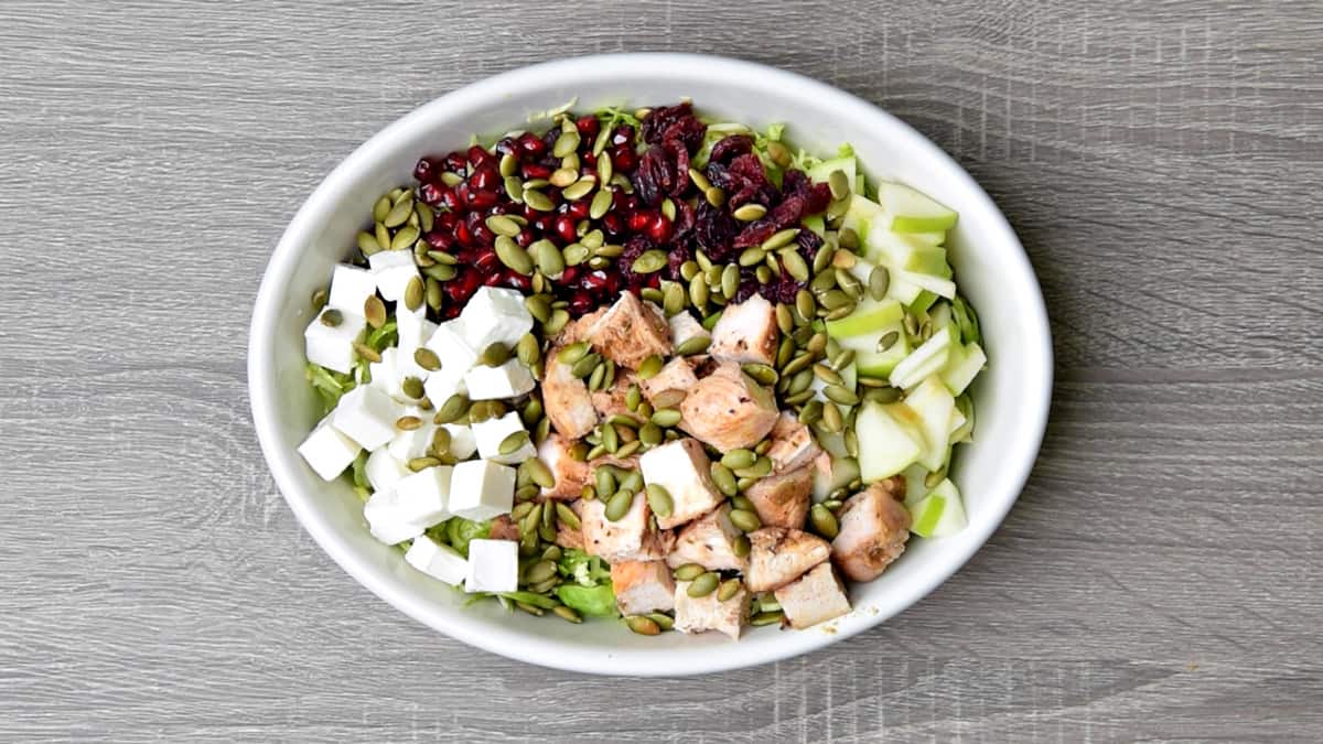 shaved brussels sprouts topped with feta cubes, pomegranate, cranberries, toasted pepitas, chicken and apples prior to tossing